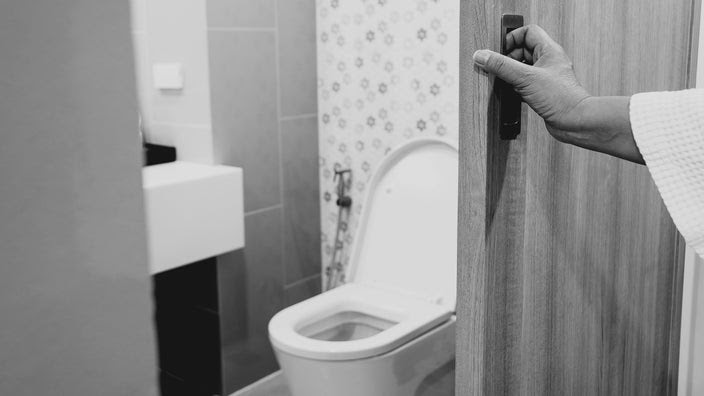 Black and white image of a person's hand opening the bathroom door.