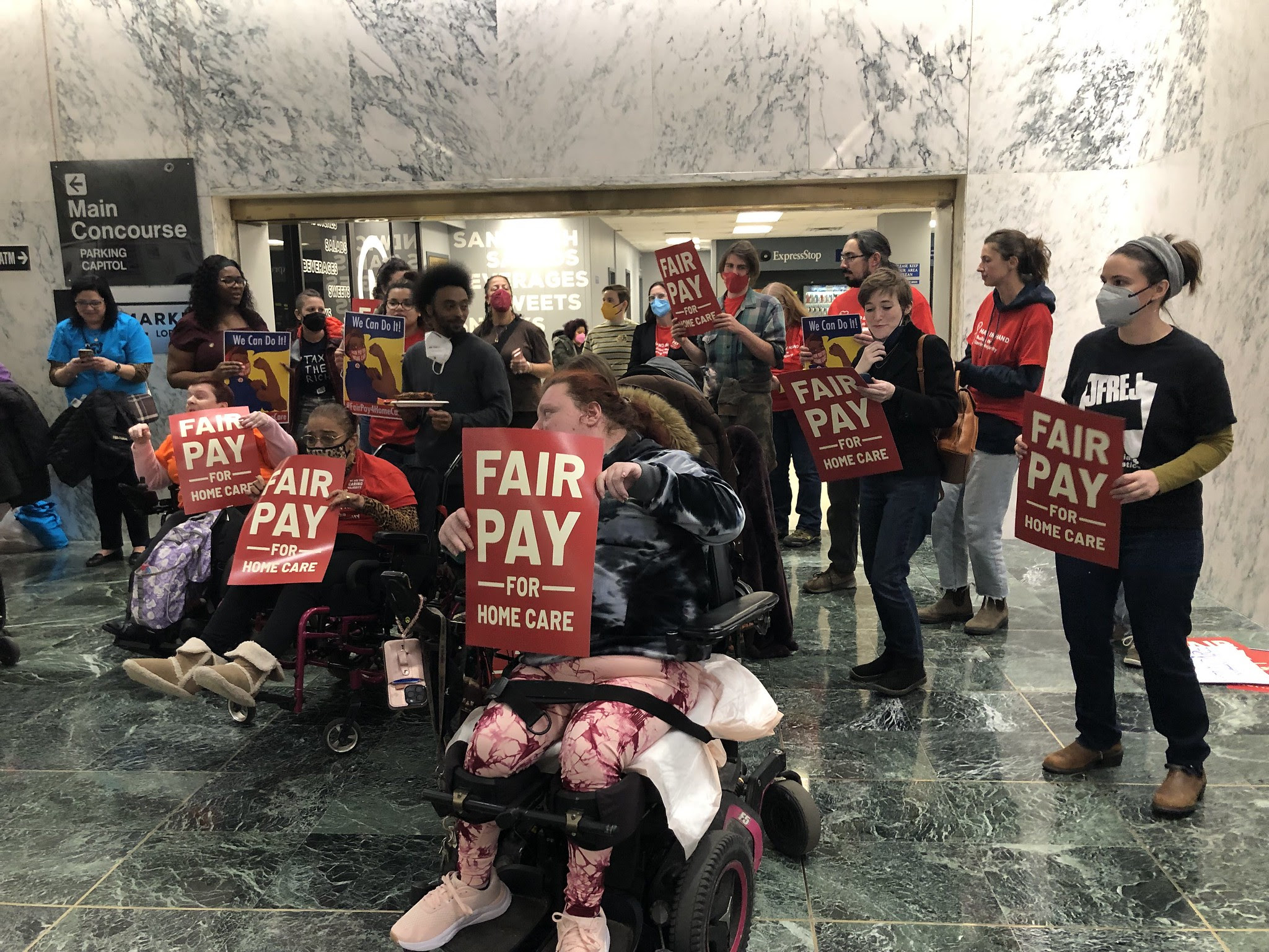 Photo of a group of people, half of them in wheelchairs, holding fair pay for home care signs