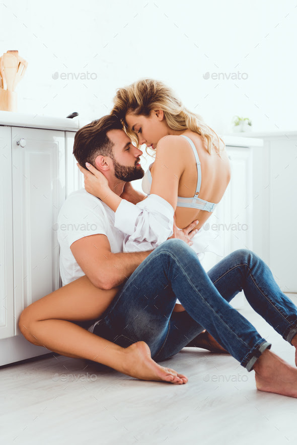 young couple embracing while sitting on floor in kitchen Stock Photo by  LightFieldStudios