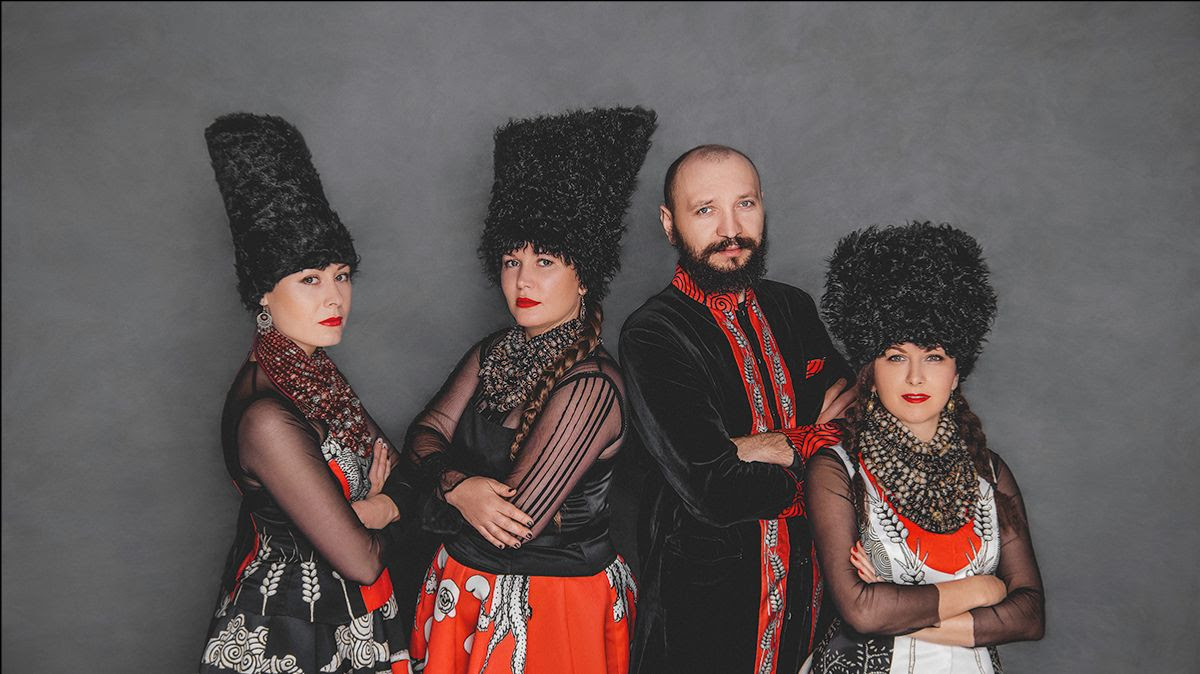 Three woman and a man wearing traditional Ukranian dress in red, black and white. The women wear tall black fur hats