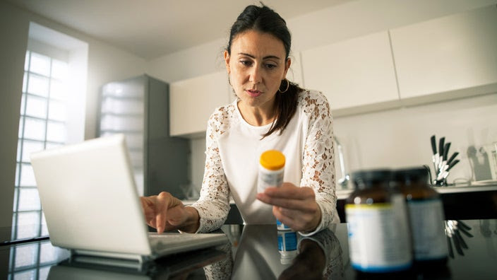 Woman looking very focused as she reviews her prescription bottle in her kitchen.