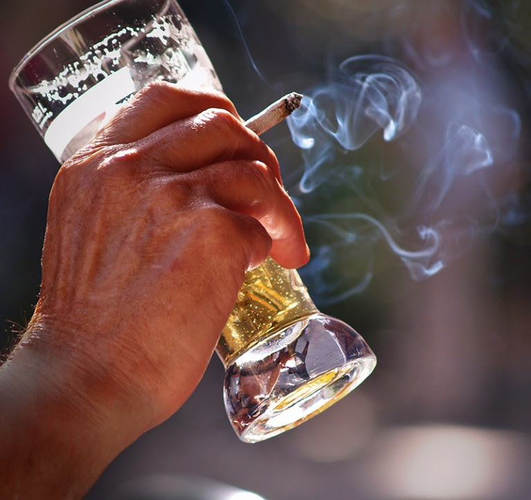 Hand holding a glass of beer and lit cigarette