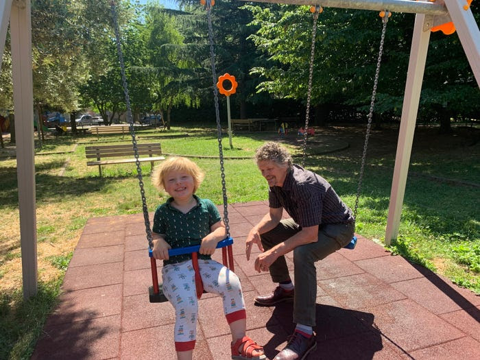 Two-year-old Barnaby Brownsell plays on a swing in a playground as his father, Peter, sits on the next swing and looks on.