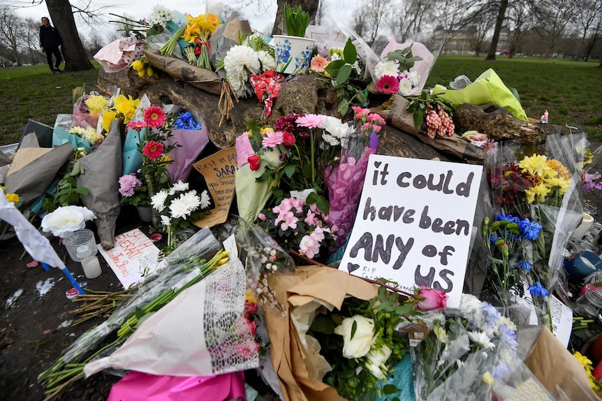 A bunch of flowers piled in a park near a sign reading 'It could have been any of us'