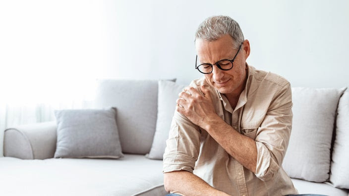 Middle aged man with shoulder pain. He is sitting on the couch.