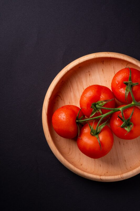 5 red tomatoes still on the vine, sitting on a wood bowl