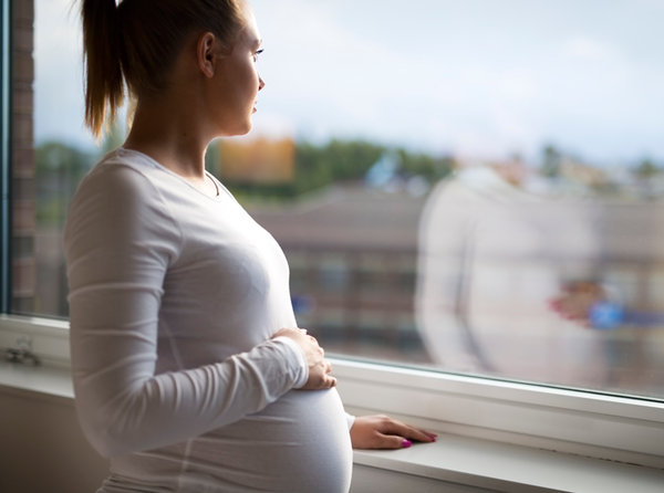 Concerned pregnant woman looks out window