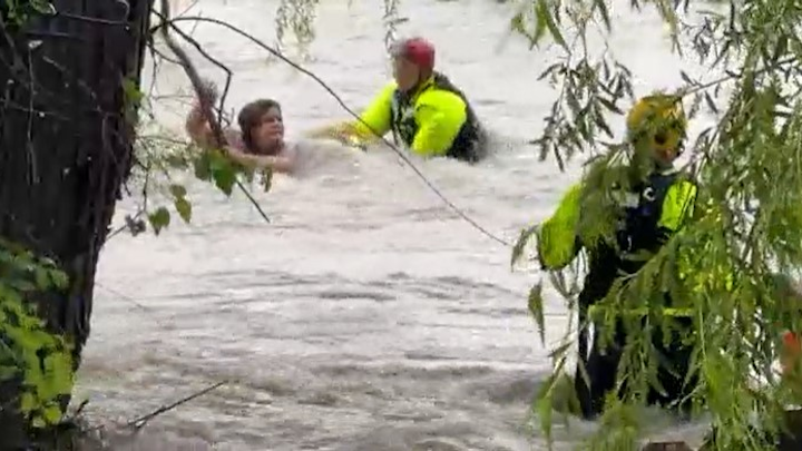 Two rescuers attempting to rescue a who was woman swept away in flood waters 