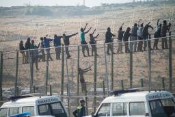 Would-be immigrants sit atop a border fence&nbsp;&hellip;