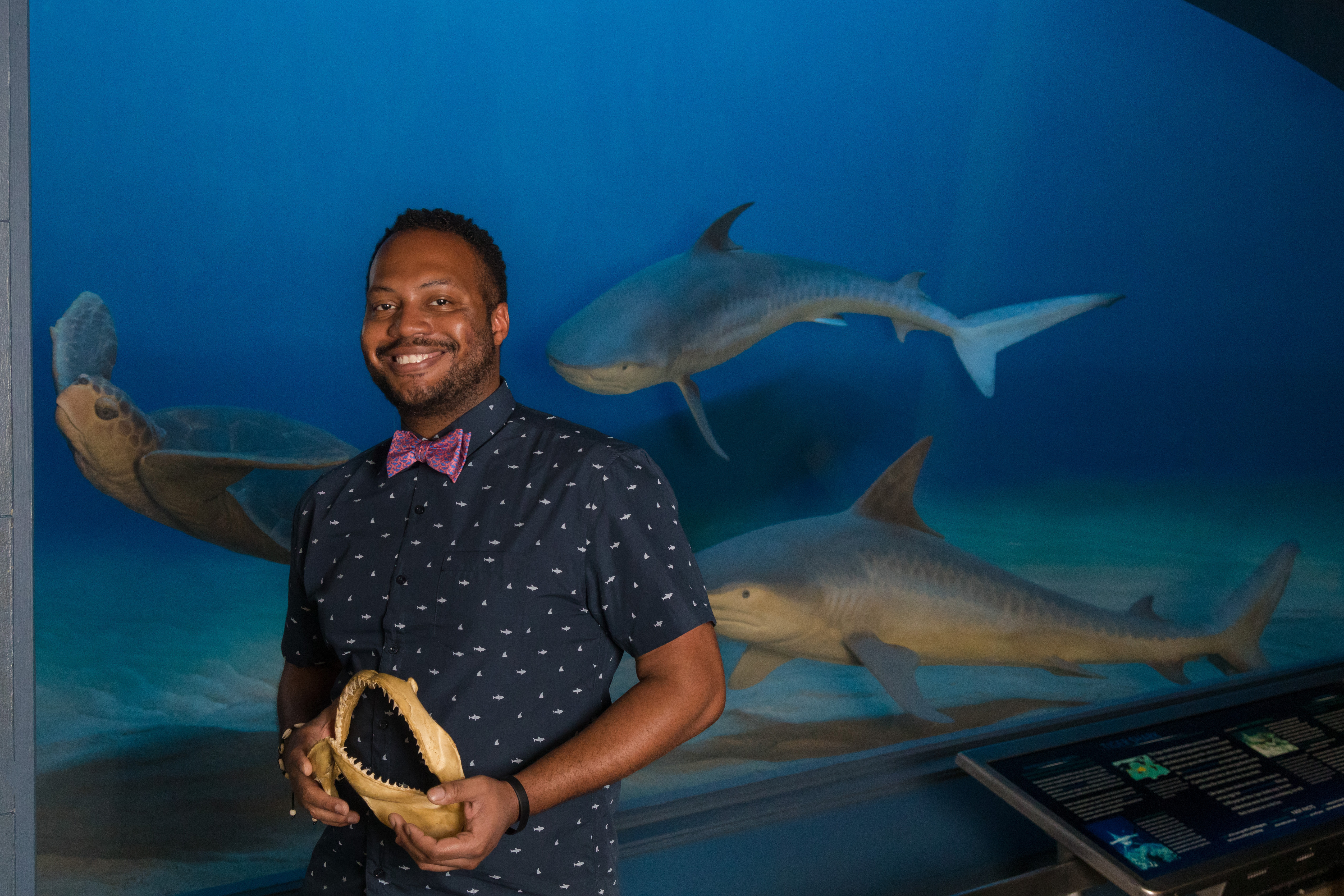 Nickcoles Martinez stands in front of a water-filled tank with sharks and a turtle.
