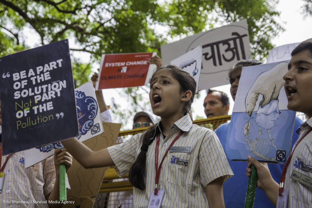 A young girl holds a sign that says "be a part of the solution not the pollution" in New Dehli (India) surrounded by other impassioned children