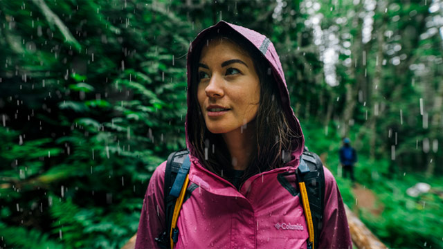 A woman stands in the rain wearing a pink OutDry Hybrid Jacket. 