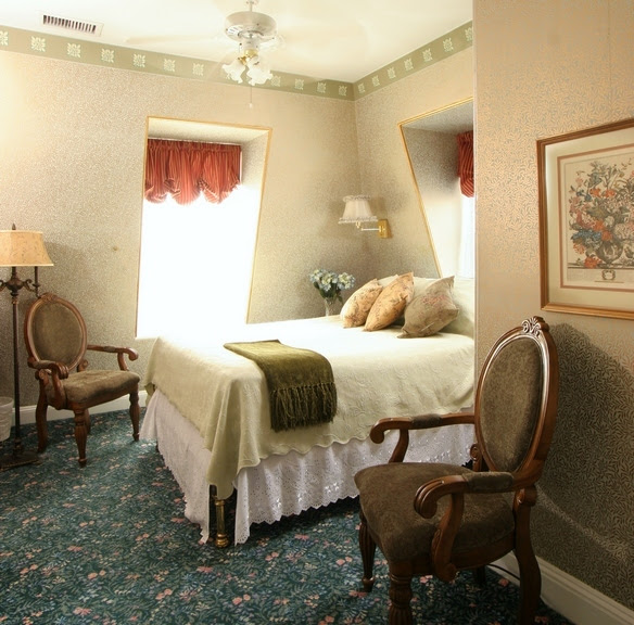 Picture of a Queen sized antique oak bed in a cheery room with yellow walls and rich green carpet.