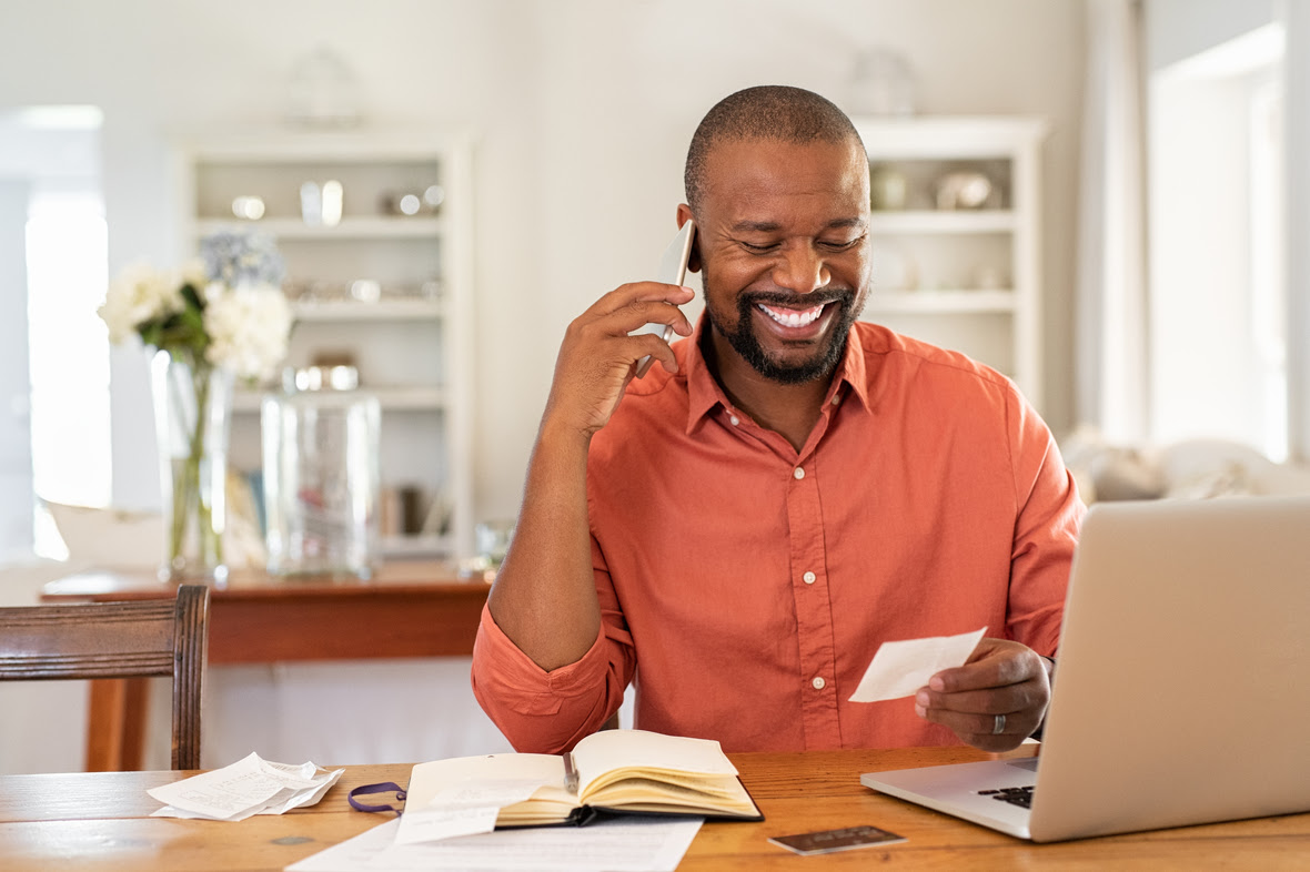 Happy-man-reading-invoice-and-talking-on-phone-1152602517 6880x4584