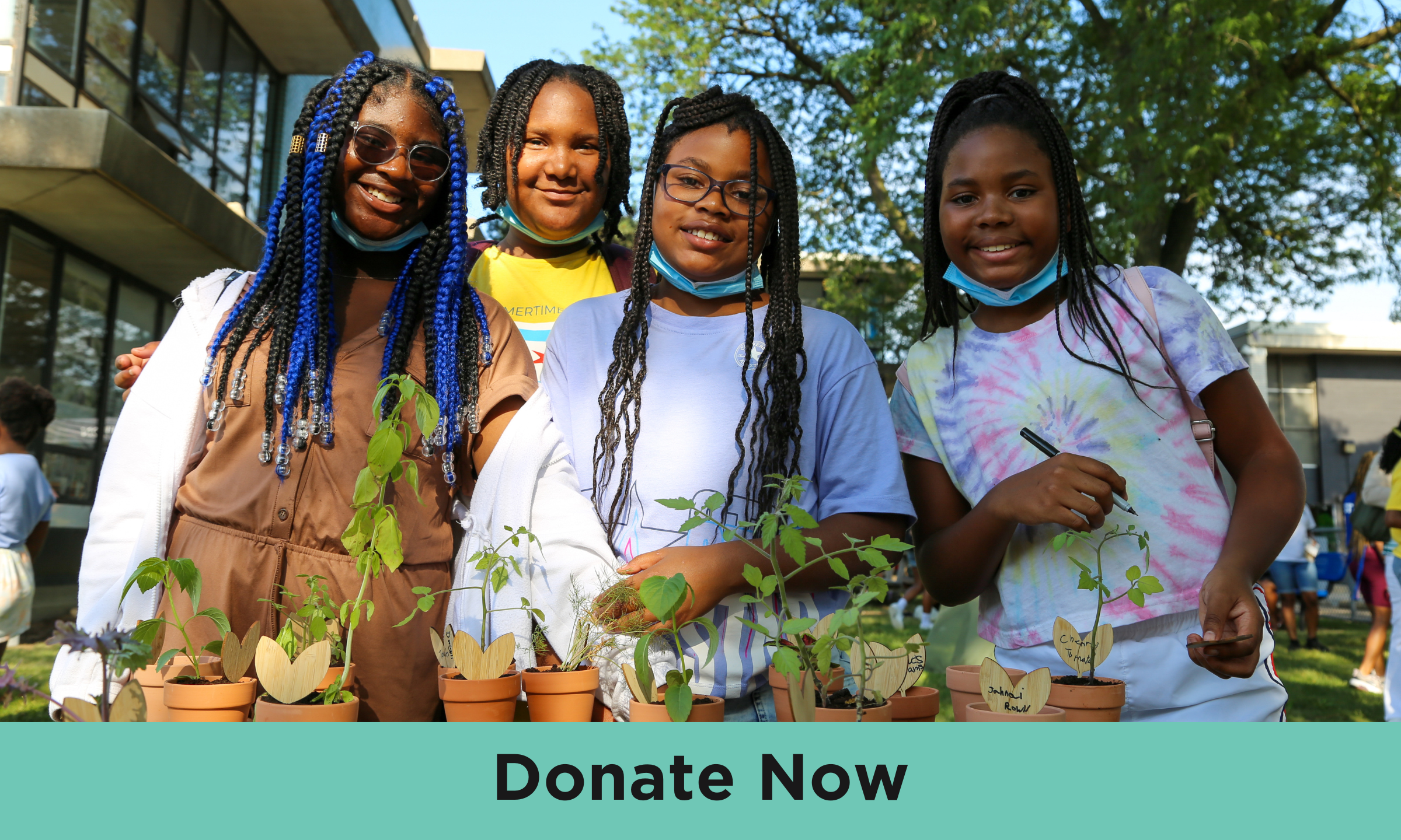 Four young people with medium-dark skin and various lengths of braided hair are standing together outside and smiling at the camera. They’re standing in front of a variety of small potted plants. At the bottom of the image are the words “Donate now”. 