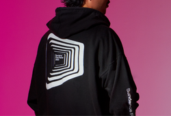 A man wearing a black festival branded hoodie against a pink background.