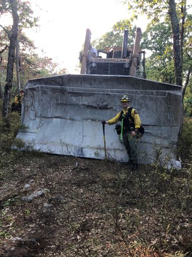 Ranger stands in front of large bulldozer in the woods
