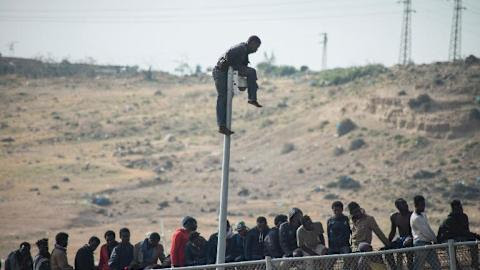 Would-be immigrants sit atop a border fence separating Morocco from the north African Spanish enclave of Melilla on May 1, 2014