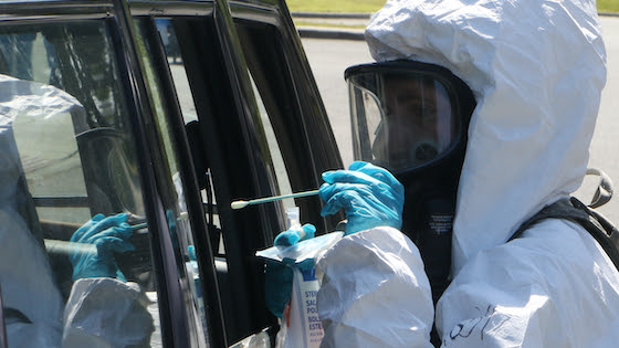 A health worker collects a swab from a driver at a drive-thru COVID-19 testing site