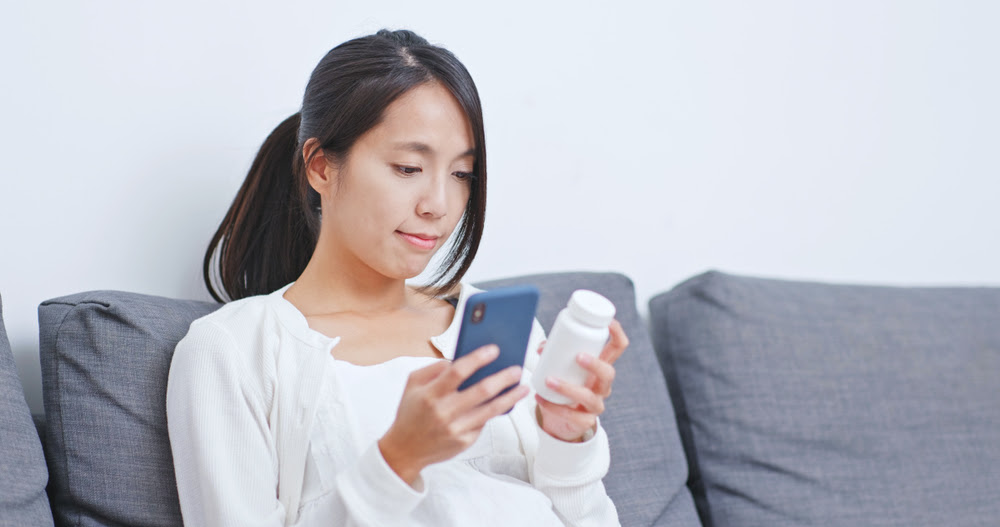 asian woman reading medication bottle and cell phone
