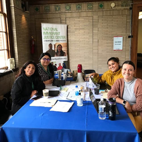 Four women legal volunteers sitting at a table in a community building, smiling and ready to help assist people.