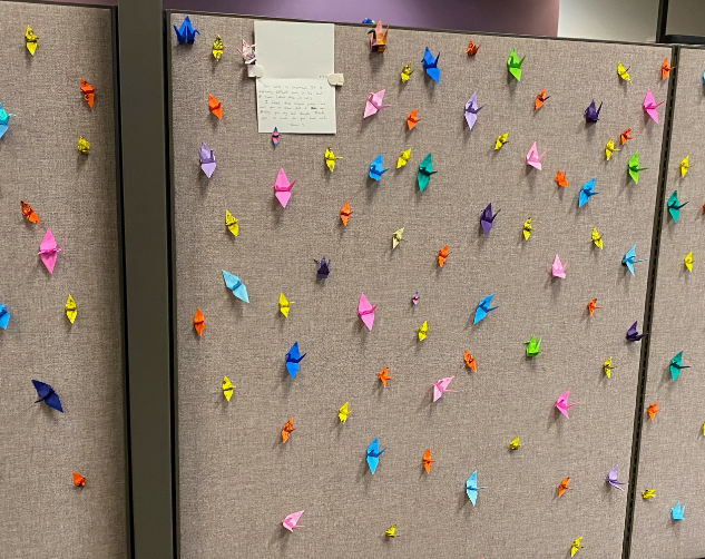 Picture of paper cranes pinned all over a cubicle wall.