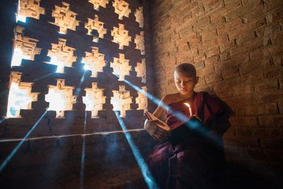 Burmese novice reading the Buddhist book inside ancient temple in Bagan plain, Myanmar.