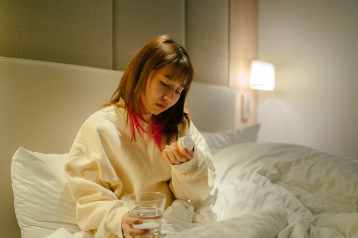 Portrait of a woman in bed looking at her prescription bottle. She has a sad and frustrated expression on her face.