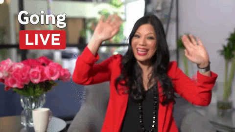 A gif of a woman in a black shirt and red jacket waving both hands next to the words "Going Live"