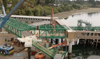 Crane and construction equipment lowering a bridge span into place atop concrete pillars at Bainbridge terminal