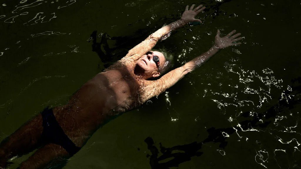 An older man wearing goggles swims in a pool