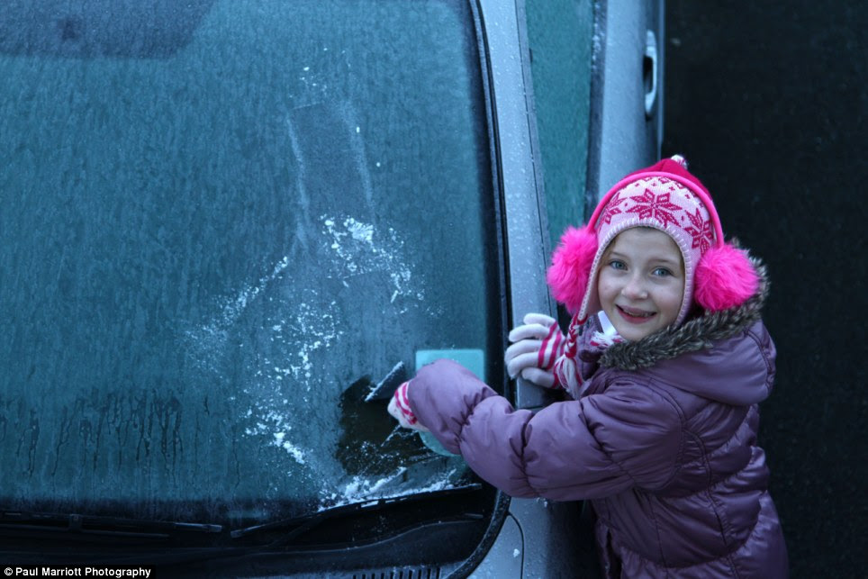 Helping hand! Georgia Marriott, 9, scrapes the ice from her mother's car on a frosty morning in Peterborough, Cambridgeshire