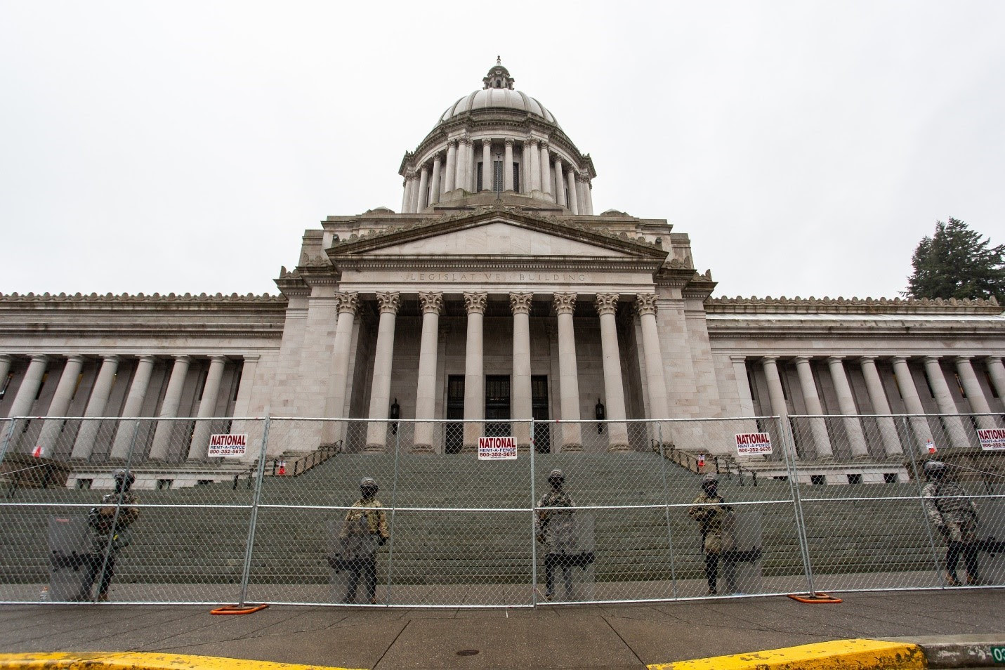 National Gurad soldiers stand behind a fence in front of the Washington State Capitol