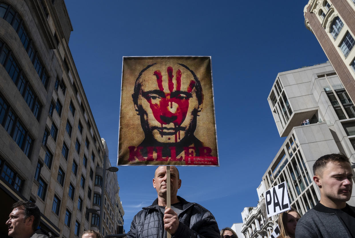 A protester in Madrid holds a placard showing the face of Russian President Vladimir Putin covered with an imprint of a bloody hand, with the word