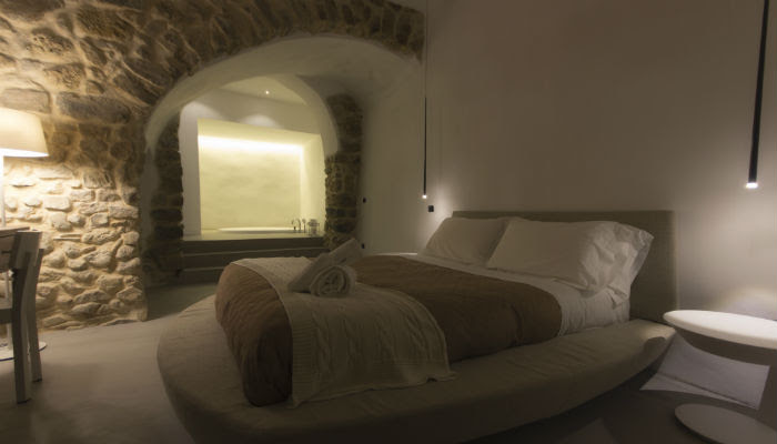 Pasqua in Sicilia - una camera d'albergo con un letto rotondo con lemnzuola bianche e copriletto beige e sullo sfondo i muri in pietra, fatti a d arco