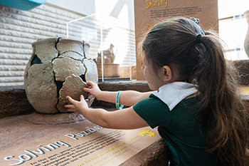 a young girl places a puzzle piece on a gray and black vase puzzle, which is upright on a wooden table
