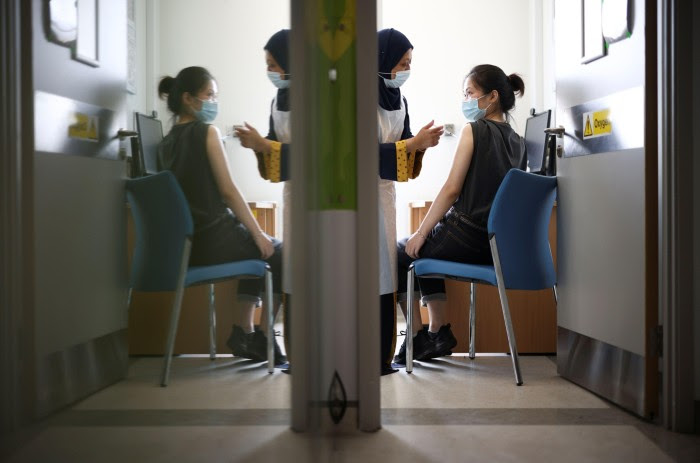 A person receiving a dose of COVID-19 and a healthcare worker are reflected in a wall creating a mirror image