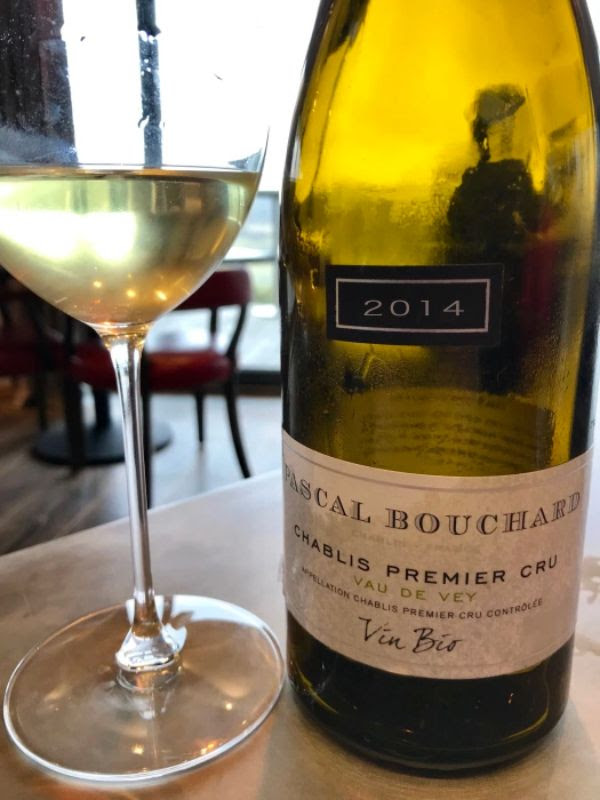 A bottle of Chablis Premier Cru Vau de Vey next to a glass of white wine.