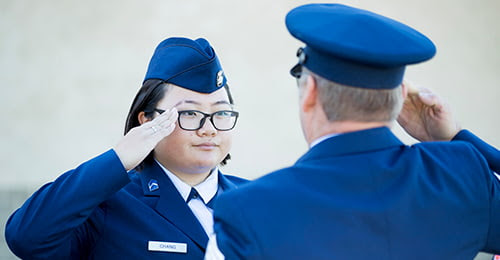 A female student in uniform salutes a uniformed officer.