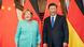 Foto registra Angela Merkel e Xi Jinping, ambos sorrindo, em frente a bandeiras da Alemanha e da China.