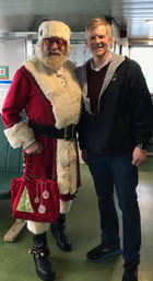 Two people standing inside the passenger cabin of a ferry posing for a photo with one of them dressed as Santa