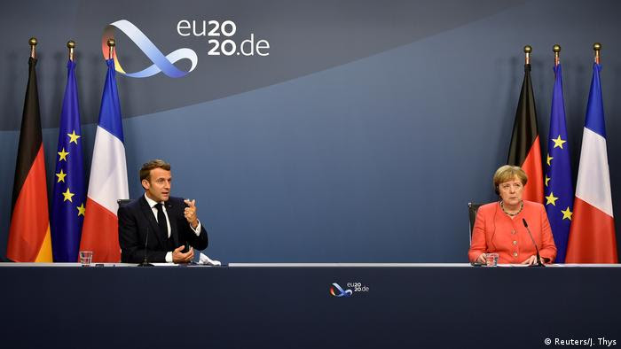 Emmanuel Macron e Angela Merkel em longa mesa, ao fundo as bandeiras da Alemanha, França e UE 
