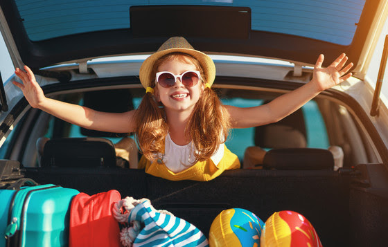 Happy child girl in car going on summer vacation trip 
