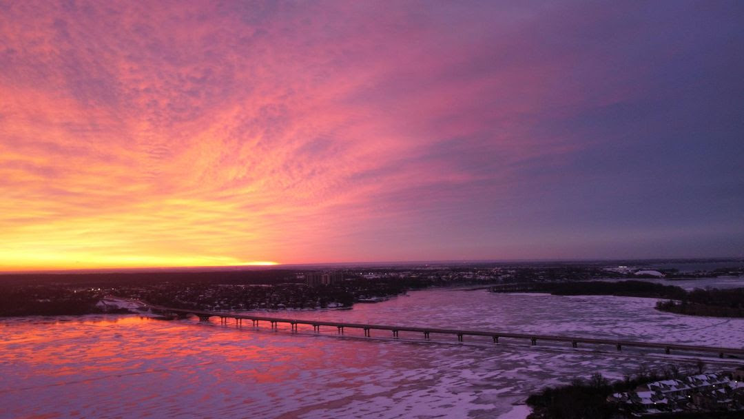 A multi-colour sunrise in orange, pink and purple hues. A bridge and river are visible in the foreground.