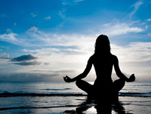Woman sitting on the beach at dusk meditating.