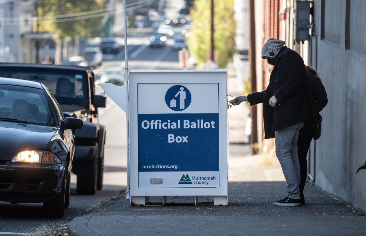 Voters return ballots to an Official Ballot Drop Box at the elections office from both the sidewalk and their cars.