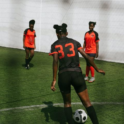A group of three women in black and orange uniforms play soccer