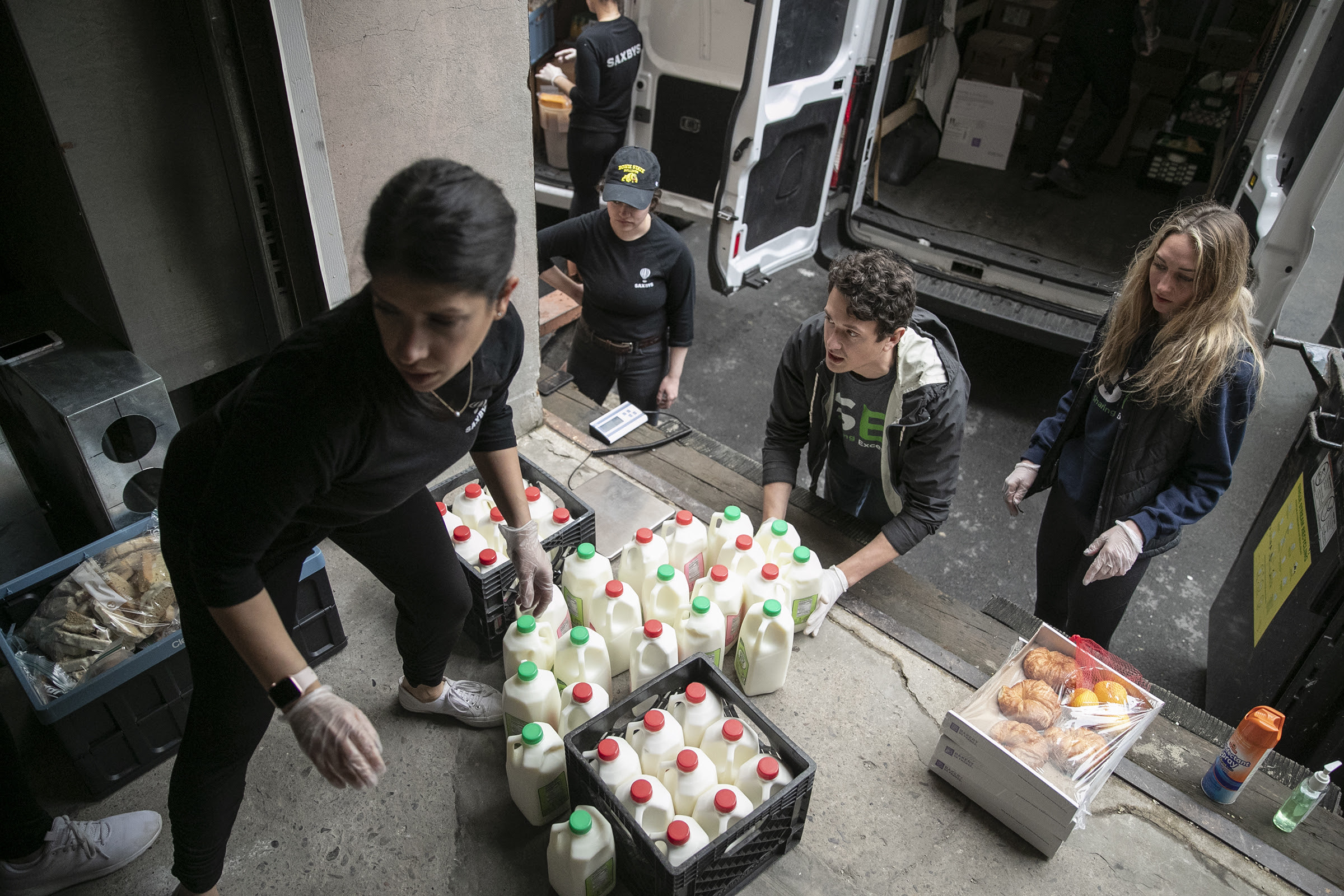 Evan Ehlers (right) founder of Sharing Excess, a Philadelphia-based nonprofit that helps connect grocery stores and restaurants with surplus food to hunger-relief organizations with storage space, lifts up milk to weigh and load in a truck from Saxby's employee Haley Samsi (left) in Center City earlier this month. Sharing Excess has received much more food than usual due to restaurants closing from the spread of the coronavirus.