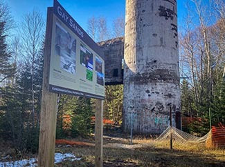 A sign interpreting the history of the stamp sands is show at the base of the smokestack from the Mohawk Mill.