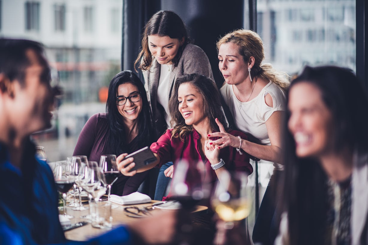 People crowding around someone with a phone at a restaurant People crowding around someone with a phone at a restaurant